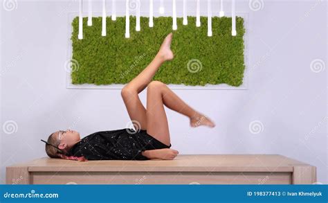 Barefoot Girl In Shining Jacket Swings Legs Lying On Table Stock Video