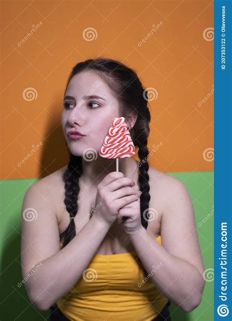 Charming Brunette Woman In Yellow Top Holding Red Big Lollipop On