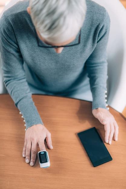 Mujer mayor usando oxímetro de pulso y teléfono inteligente que mide la