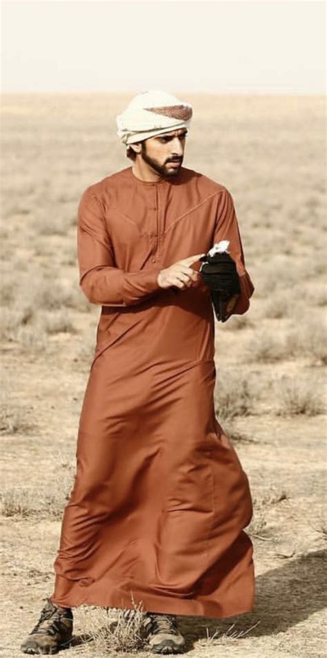 A Man In An Orange Outfit Is Standing In The Desert With His Hands