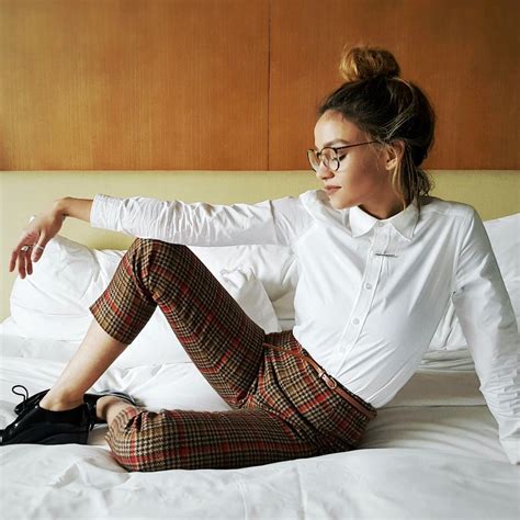 A Woman Sitting On Top Of A Bed Wearing Plaid Pants And White Shirt