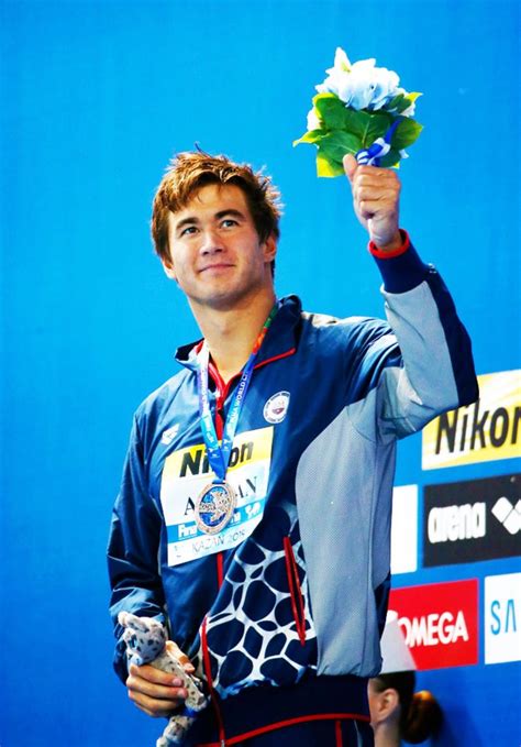 A Man Holding Up A Flower While Standing On Top Of A Blue Wall With His Hands In The Air