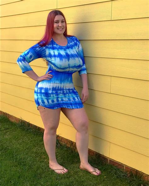 A Woman Standing In Front Of A Yellow Wall Wearing A Blue Tie Dyed Dress
