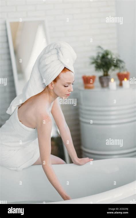 pretty slim woman wrapped in towel preparing bath at home sitting on edge of bathtub filling up