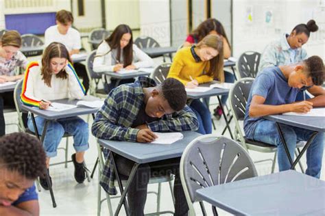 Focused High School Students Taking Exam At Desks In Classroom Stock