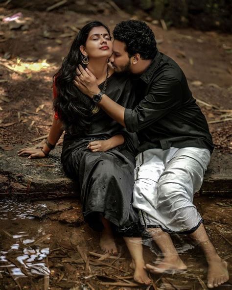 A Man And Woman Sitting Next To Each Other On The Ground In Water With Trees Behind Them