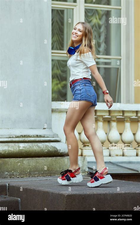 Smiling Russian Girl In Denim Shorts And Platform Shoes Is Dancing Near Facade Of A Historic