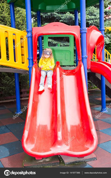 Happy Adorable Girl On Childrens Slide On Playground Near Kindergarten