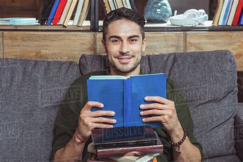 Handsome Male Student Reading Books And Smiling At Camera Stock Photo