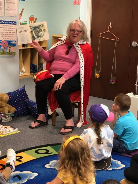 An Older Woman Sitting In A Chair Reading To Children