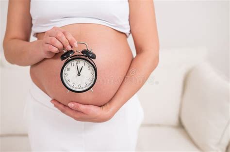 A Pregnant Woman With A Naked Belly Holds An Alarm Clock Intended Date Of Birth Stock Image