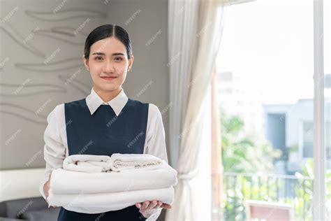 jovem asiática empregada doméstica de uniforme segurando toalhas brancas e limpas no quarto do