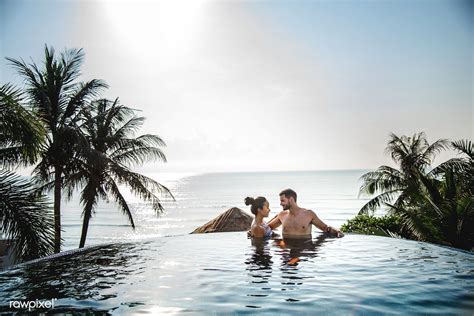 A Man And Woman Are Sitting In The Pool Near The Water With Palm Trees Around Them