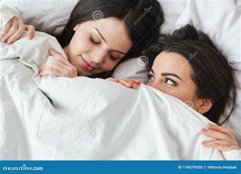 Lesbian Couple In Bedroom At Home Lying Under Blanket One Woman Sleeping Another Looking At Her