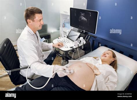 Smiling Male Doctor Obstetrician Examining Belly Of Happy Pregnant Woman By Ultrasonic Scan