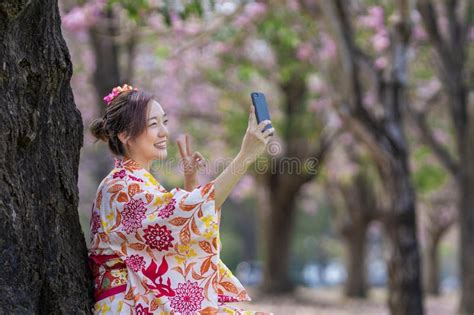 Japanese Woman In Traditional Kimono Taking Selfie With Peace Gesture While Walking In The Park
