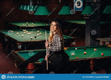 A Girl In A Hat In A Billiard Club Sits On A Billiard Table With A Cue