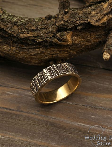 A Gold Wedding Ring Sitting On Top Of A Wooden Table Next To A Tree Branch