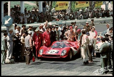 A Group Of Men Standing Around A Red Race Car In Front Of A Large Crowd