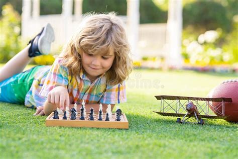 Kid Playing Chess Game In Backyard Laying On Grass Concentrated Child