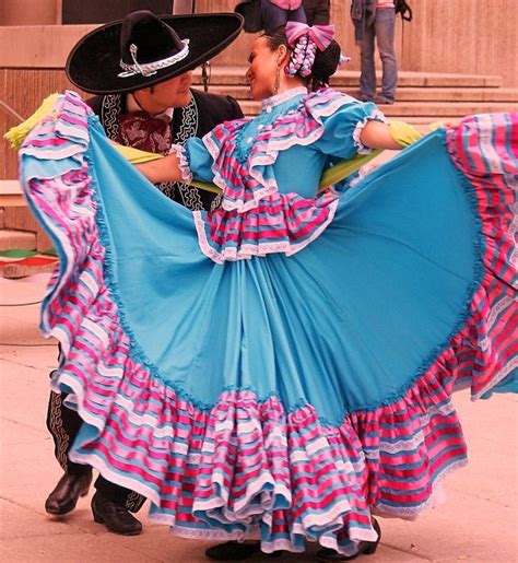 two people dressed in mexican attire dancing on the street