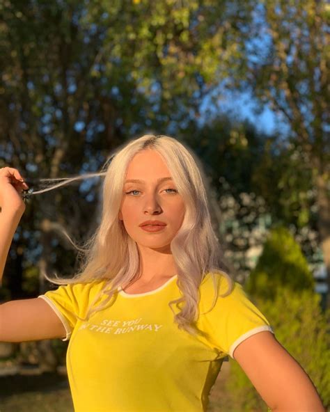 A Woman In A Yellow Shirt Holding Scissors To Her Hair