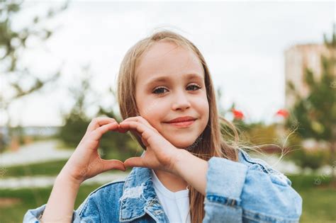 premium photo a little blonde girl shows a heart sign made with her fingers while standing on
