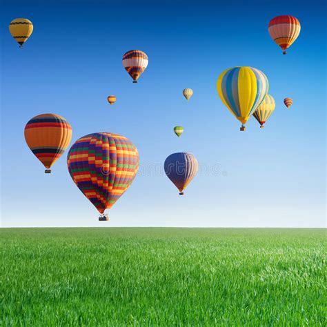 Hot Air Balloons Flying In Blue Sky Above Green Field Stock Photo