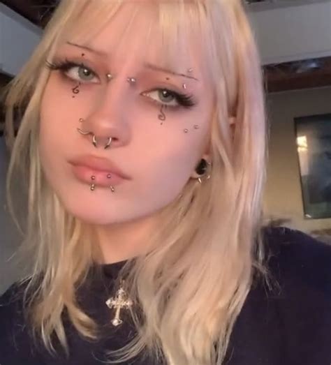 A Blonde Woman With Piercings On Her Face And Nose Is Looking At The Camera