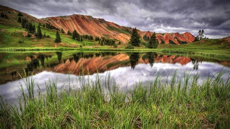 Red Mountains Perfectly Reflected In Small Lake Dramatic Stormy Skies