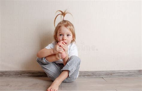 A Little Girl Bites Her Toenails While Sitting On The Floor Of A Room