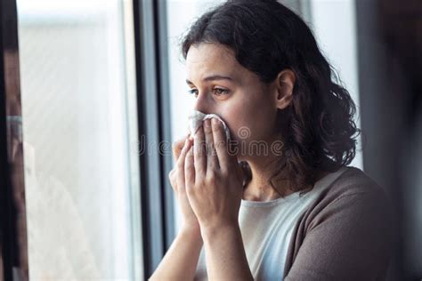 Sad Young Woman Crying While Looking Through The Window At Home Stock