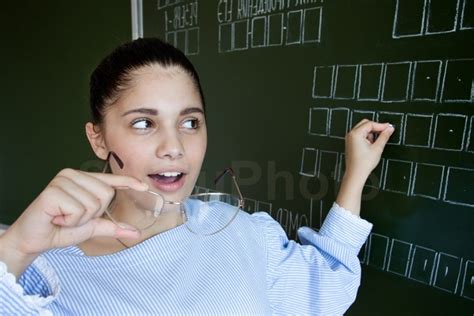 Student Writing On Blackboard With Chalk In Classroom