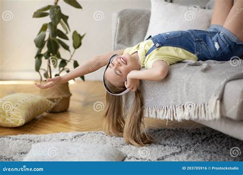 Teenage Girl Lying Upside Down On Couch Listening To Music Stock Photo