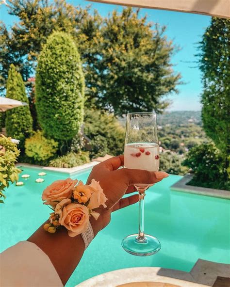A Person Holding A Wine Glass Near A Swimming Pool With Flowers On The