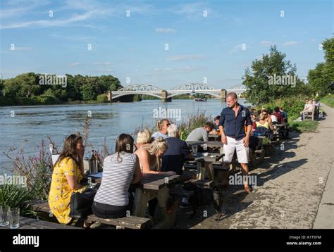 People Enjoying A Quiet Drink Next To The River Thames Outside The White Hart Pub In Barnes