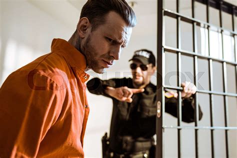 Prison Guard Showing Something To Criminal In Prison Cell Stock Image