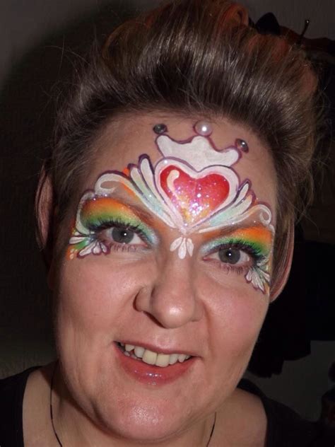 A Woman With Her Face Painted Like A Frog And Rainbows On Her Face Is Smiling At The Camera