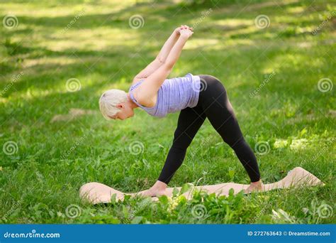 A Middle Aged Woman Practices Yoga Outdoors In The Standing Forward