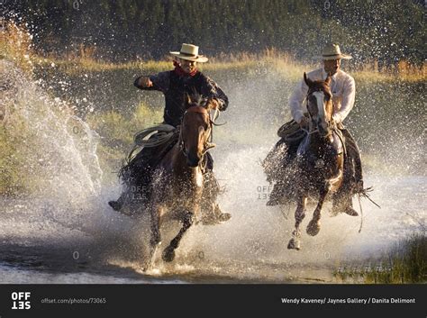 Two Cowboys On Horses Riding Through Water Stock Photo Offset