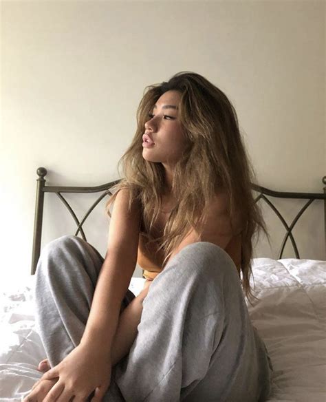 A Woman Sitting On Top Of A Bed Next To A White Wall And Wearing Grey Sweatpants