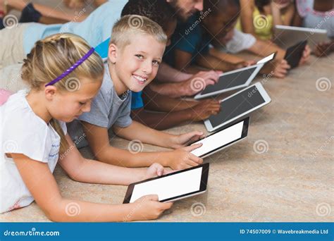 Lehrer Und Kinder Die Auf Boden Unter Verwendung Der Digitalen Tablette In Der Bibliothek