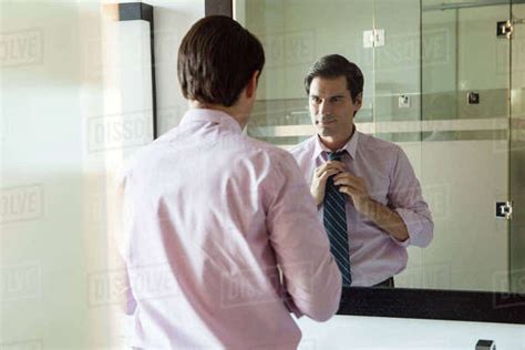 Man Looking In Bathroom Mirror Adjusting Necktie Stock Photo Dissolve