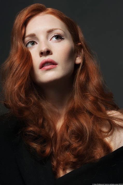 a woman with long red hair and blue eyes looking up to the side in front of a dark background