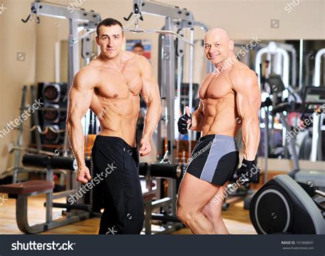 Two Bodybuilders Pose And Show Thumbs Up On Training In The Hall Stock