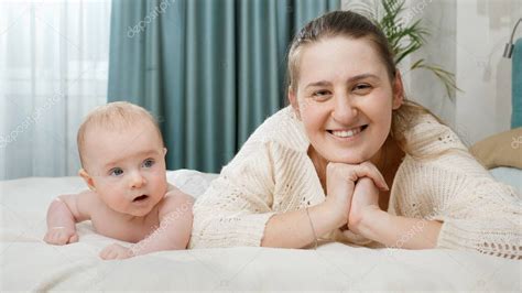 Joven Madre Feliz Sonriente Acostada Con Su Bebé En La Cama Y Mirando