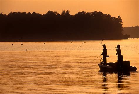Two Men Fishing Off A Boat On Toledo Bend Lake At Sunset With Passing
