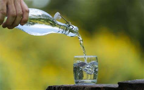 Mano Vertiendo Agua De Bebida De Botella En Vidrio Con Fondo Natural Foto Premium
