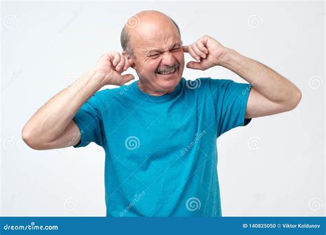 Senior Hispanic Bald Guy Plugging Ears With Fingers Hearing Loud Sounds