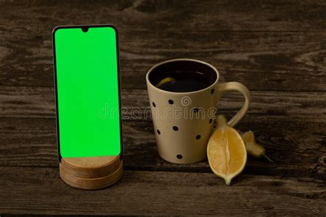 Mobile Phone With A Green Screen And A Cup Of Tea With Lemon On An Old